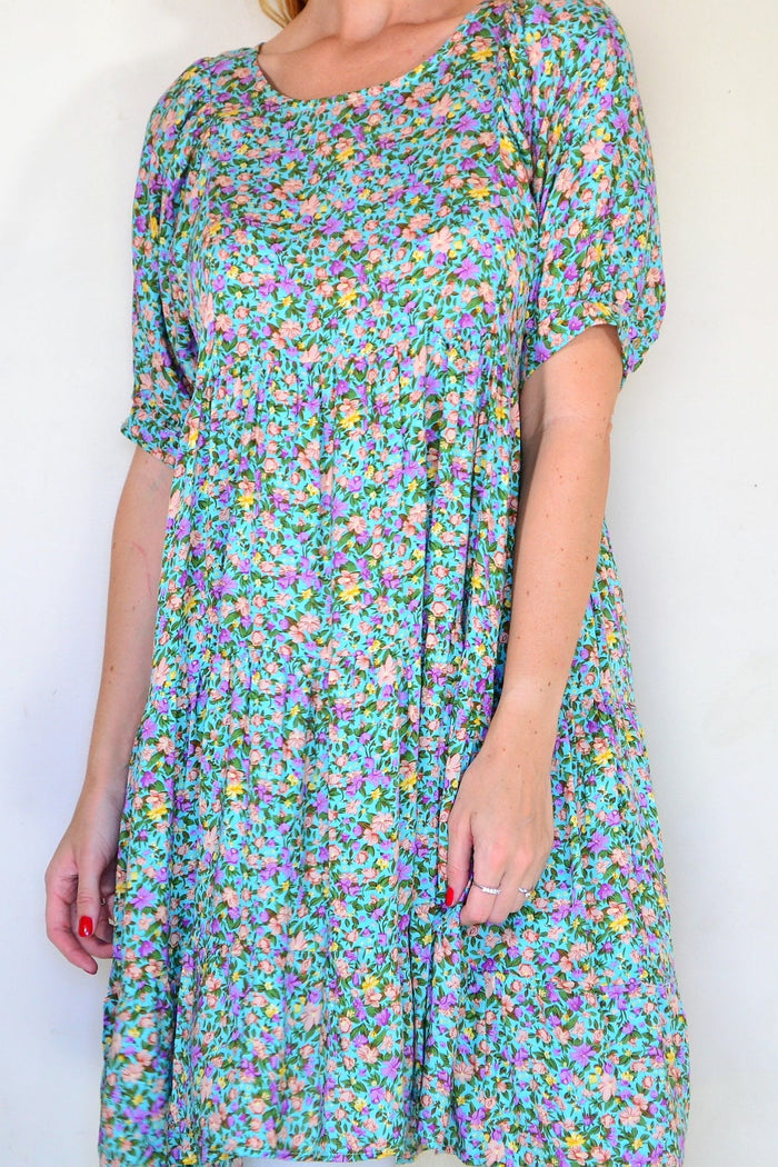 Willow Tree Aqua Flutter Tree Tunic Dress hanging on a mannequin, featuring a vibrant floral pattern and flowing fabric.