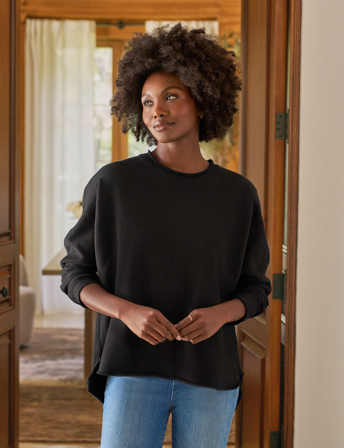 Woman wearing a black sweater and blue jeans standing in a doorway.