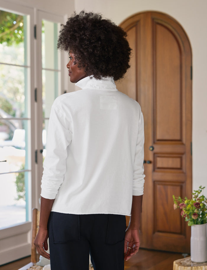 Person wearing a white shirt standing in a room with wooden doors and a plant.