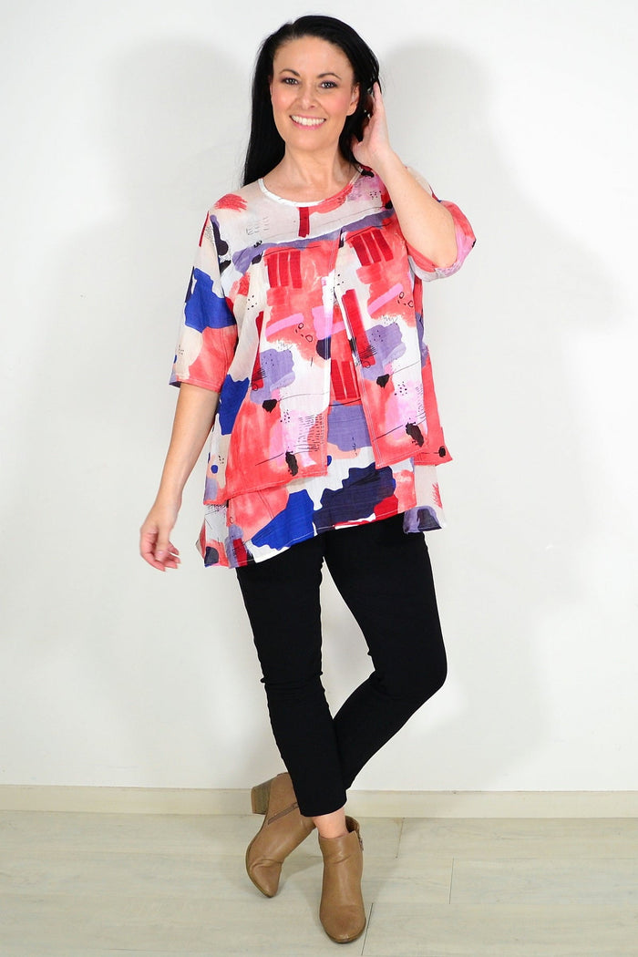 Red layered abstract tunic top by Whispers, featuring a flowing design and vibrant pattern, displayed on a hanger.