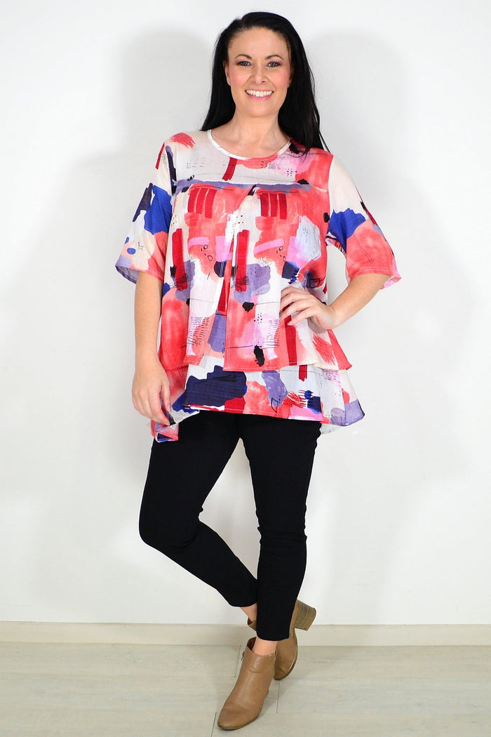 Red layered abstract tunic top by Whispers, featuring flowing fabric and artistic design, displayed on a hanger.